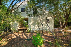 This wide view of the front exterior highlights the natural setting and additional storage space, surrounded by mature trees that frame the home with privacy. The thoughtful layout makes use of the wooded lot while creating a welcoming approach to the property.