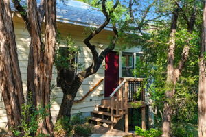 A freshly updated entryway welcomes you with steps leading to a cozy front porch, framed by mature trees for added privacy. The elevated setting creates a natural treehouse vibe while offering a warm first impression of the home.