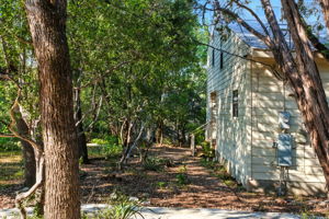 From the driveway, the side view of the home reveals its distinctive breezeway at the center of the structure, connecting the main living space with the storage area and back porch. Surrounded by mature trees, this thoughtful design blends practicality with charm, reinforcing the home’s private, treehouse-like character.