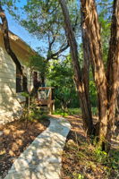 A gently curving concrete path leads you through the trees and up to the front door, immediately setting the stage for the home’s treehouse-like retreat. Surrounded by natural shade and greenery, the entry feels private and serene, welcoming you into the peaceful setting that defines this property.