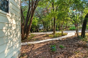 A winding concrete path leads from the home toward the driveway, framed by mature trees that provide shade and privacy. This natural approach enhances the home’s treehouse character and creates a welcoming transition between the indoors and the wooded surroundings.