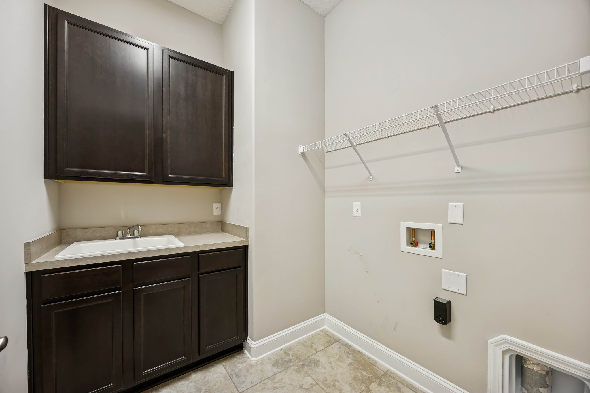 The laundry room is well-organized, with upper cabinetry, storage shelving, and a built-in utility sink ...