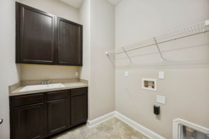 The laundry room is well-organized, with upper cabinetry, storage shelving, and a built-in utility sink ...
