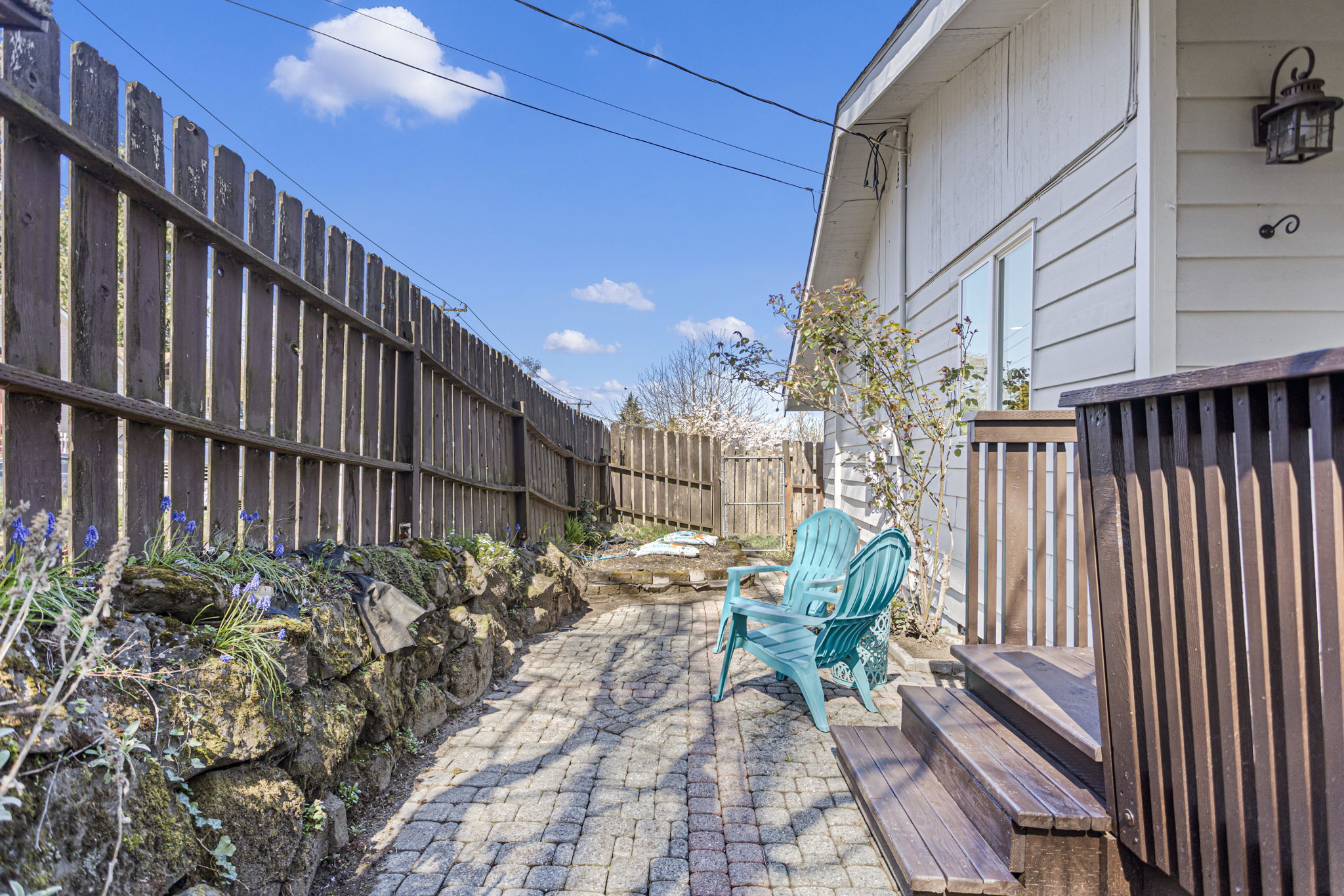 Cobblestone path from the front entry — rock border, spring bulbs already coming up, and a gate through to the back.