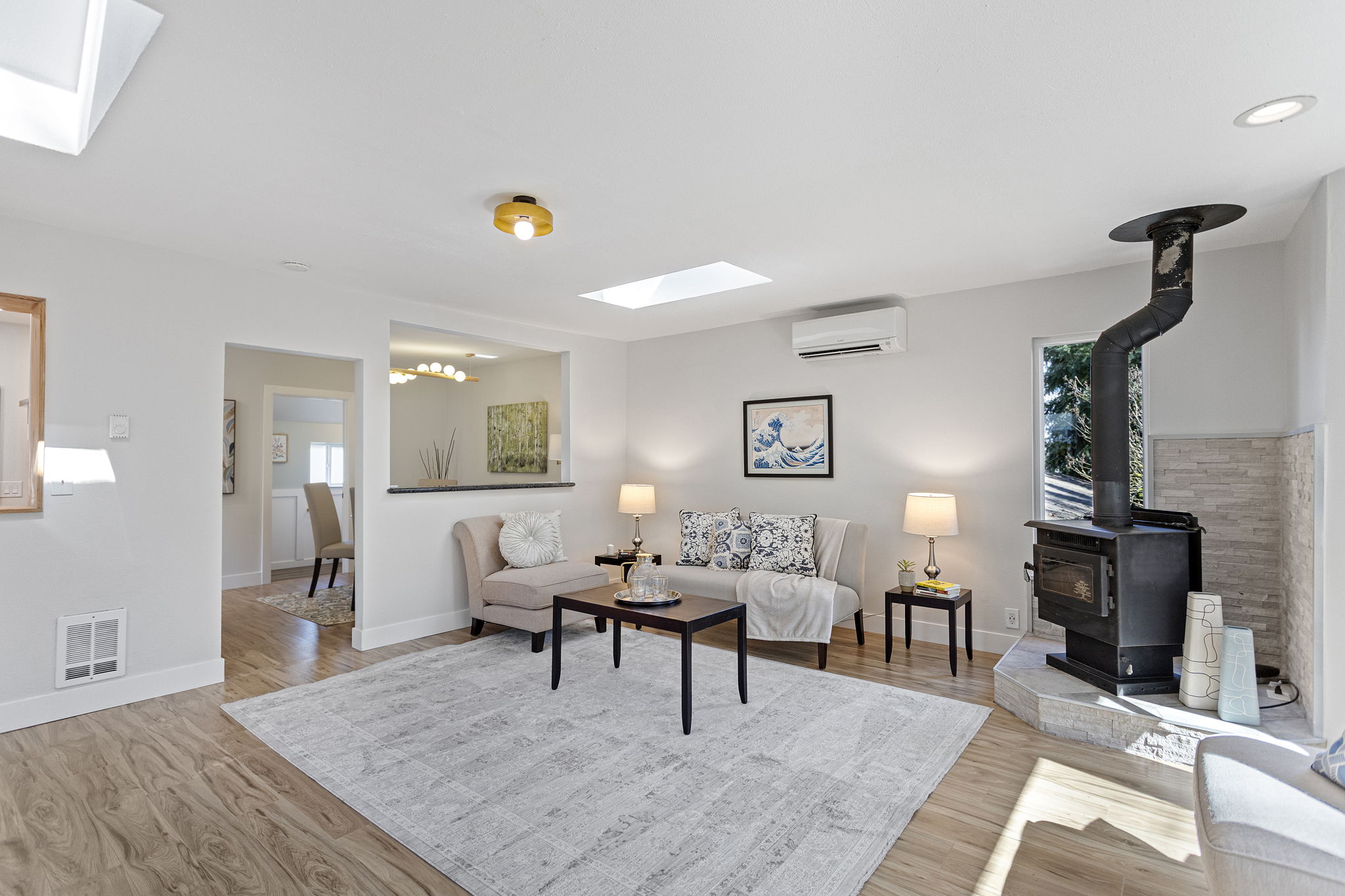 Welcome home. Two skylights pull light down into a living room that connects to everything — pellet stove in the corner, serve-through to the kitchen, open passage to the dining room.