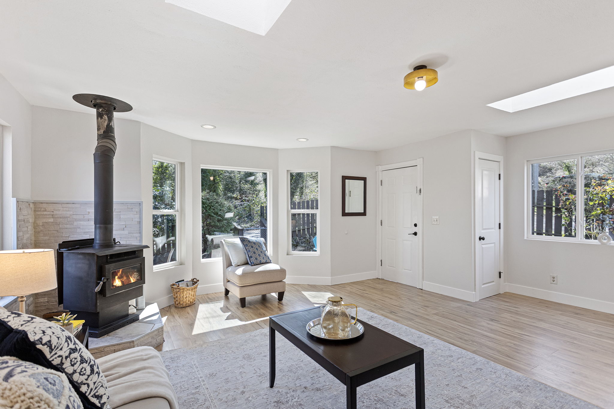 Wood stove on stacked stone, mini-split on the wall, and a south-facing bay window flooding the room with light. A living room built for every season — and looking good doing it.
