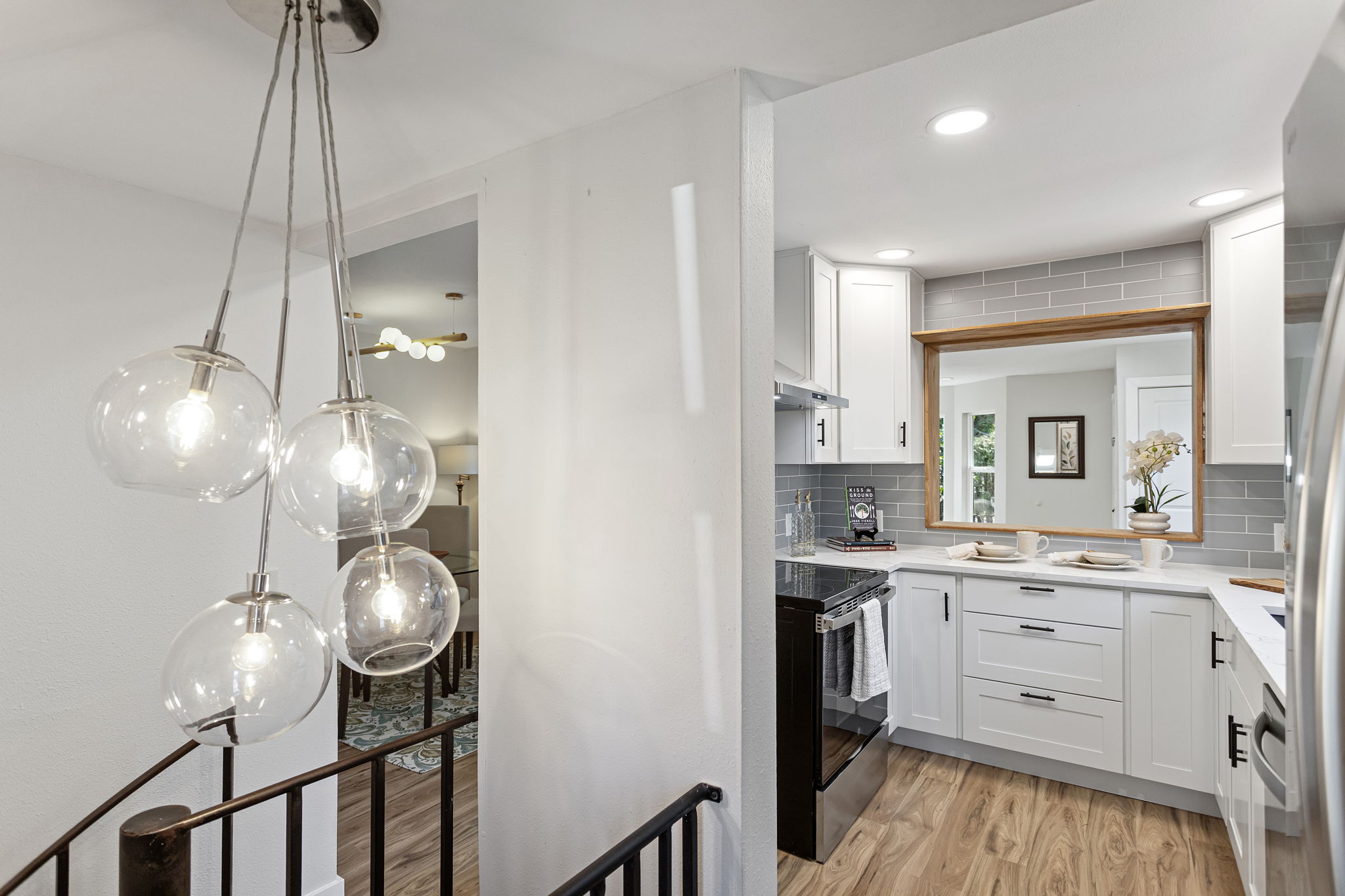 From the spiral stair landing: the globe cluster pendant, the dining room beyond, the kitchen beside it. One last look before the stairs take you down.
