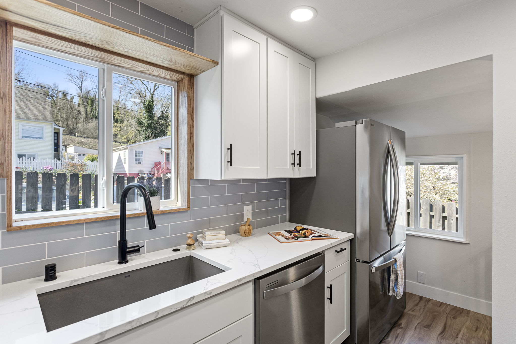 The sink wall: oak-framed west window with sill shelf, matte black faucet, quartz counters. Light lingers here longer than you'd expect.