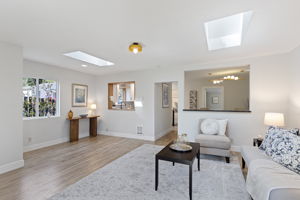 Every opening earns its place: wood-framed serve-through to the kitchen, open-cased passage to the dining room, two skylights overhead. Light moves through this room all day.