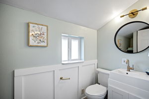 Board-and-batten wainscoting, brass fixtures, round black-framed mirror — the main floor ¾ bath punches above its square footage.