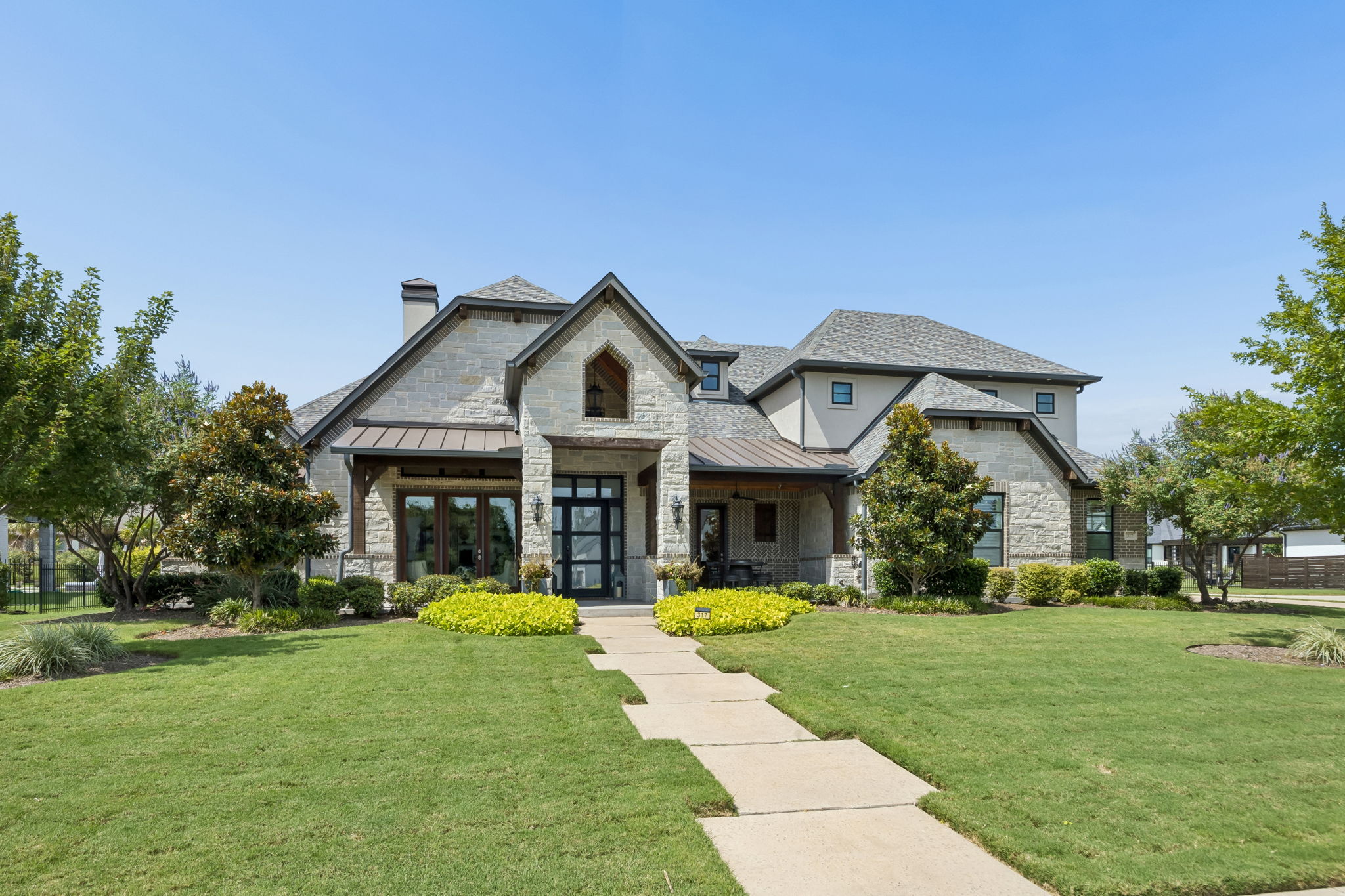 Distinctive Curb Appeal in Full Daylight – Stone, brick, stucco, metal accents, varied rooflines, and mature landscaping give the home a custom look from every angle.
