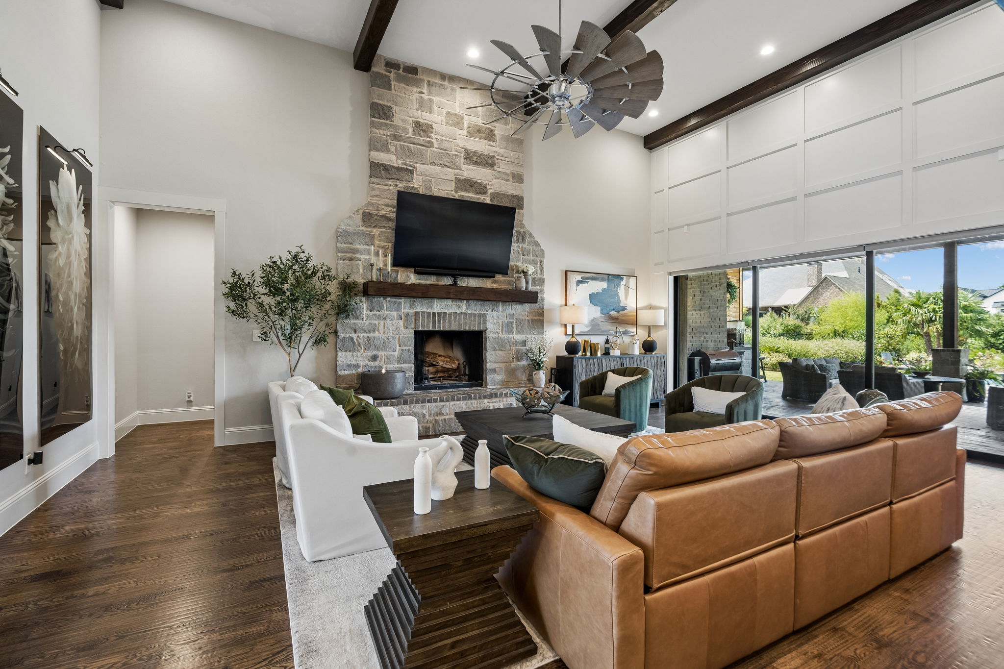 A Great Room Designed Around the View – The spacious living area is anchored by a two-story stone fireplace and framed by exposed beams, while the retractable glass wall extends the room visually and functionally toward the covered terrace and pool.