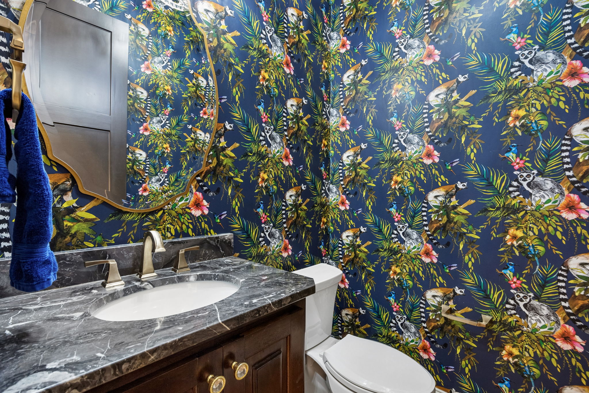 A Powder Bath with Personality – Bold botanical wallpaper, a sculptural mirror, dark stone counter, and warm metal fixtures give this guest bath a memorable, custom-designed look.