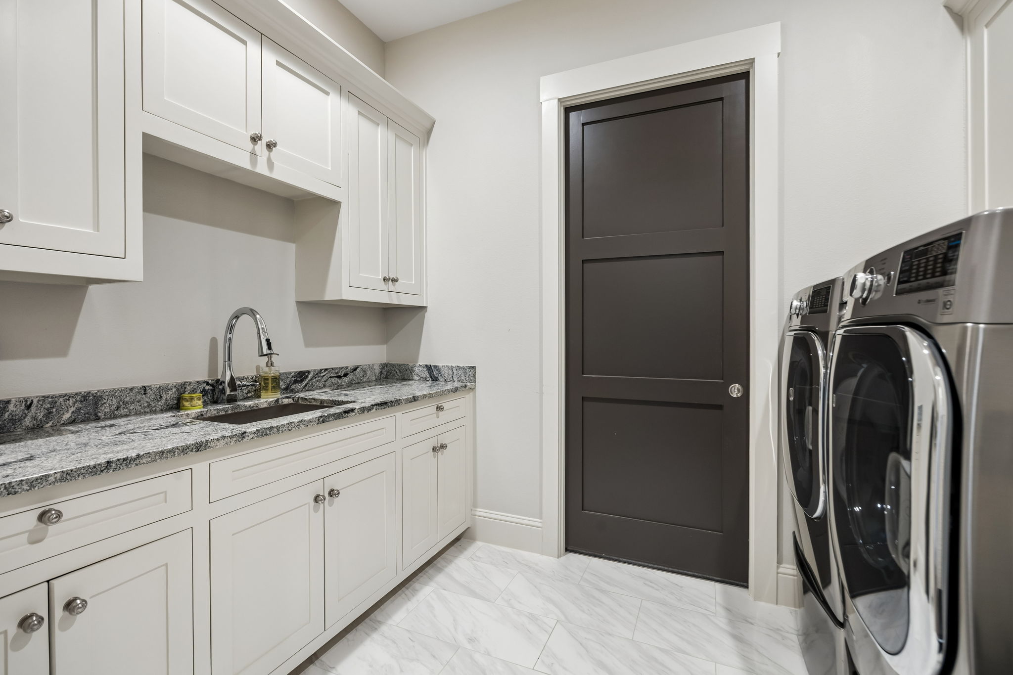 A Laundry Room Built for Everyday Efficiency – Generous cabinetry, a utility sink, extensive counter space, and room for full-size appliances create a practical workspace for washing, folding, storage, and household organization.