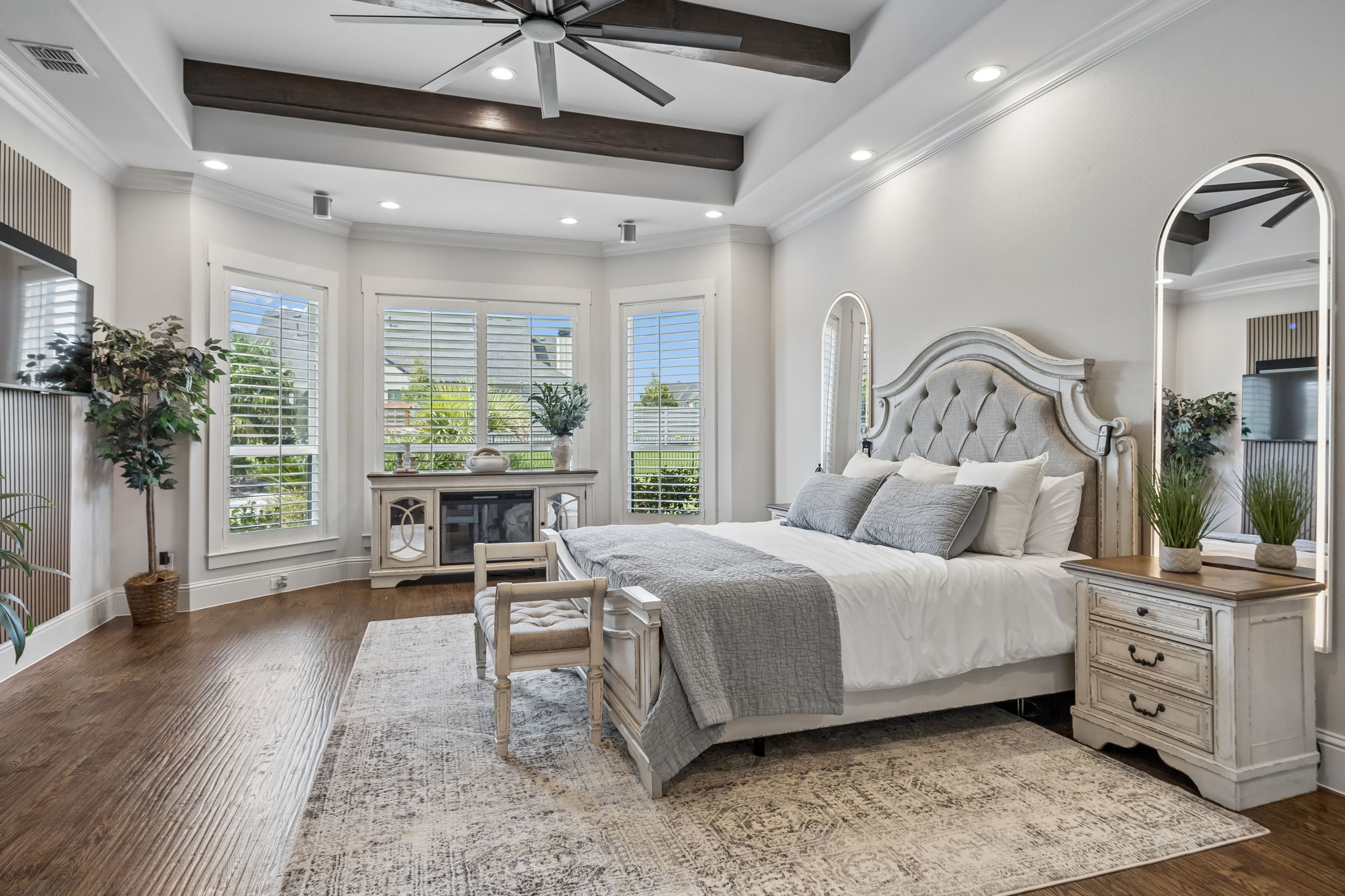 A Spacious Primary Retreat – The primary bedroom offers generous proportions, hand-scraped hardwood floors, a tray ceiling with exposed beams, and a bay of windows that brings in natural light and backyard views