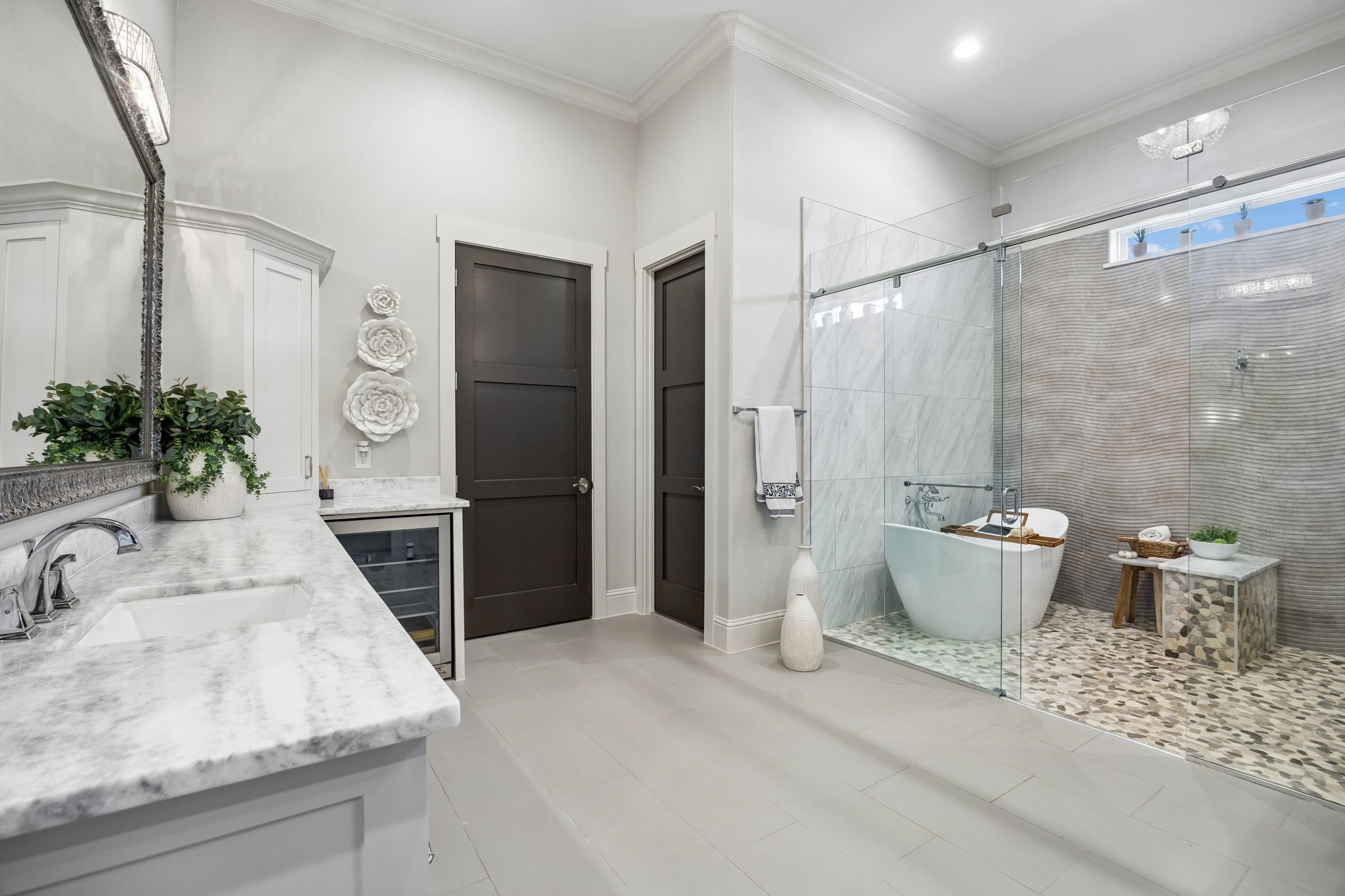 A Spa-Inspired Wet Room – The primary bath features a glass-enclosed wet room with a freestanding soaking tub, multi-head shower, pebble flooring, textured tile, and natural light for a relaxing retreat at home.