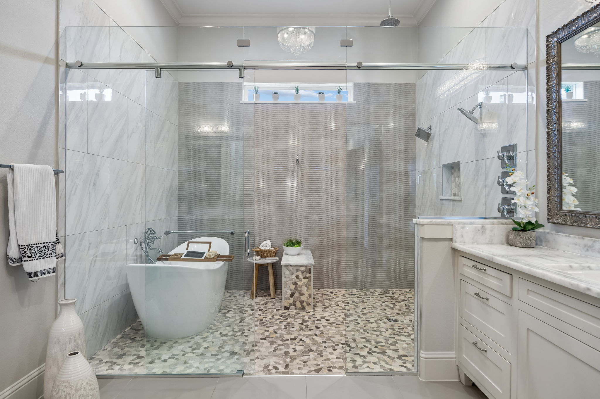 A Wet Room Designed for a True Spa Experience – The oversized glass enclosure brings together the freestanding soaking tub, dual shower stations, handheld fixtures, pebble flooring, and textured tile in one dramatic bathing space.