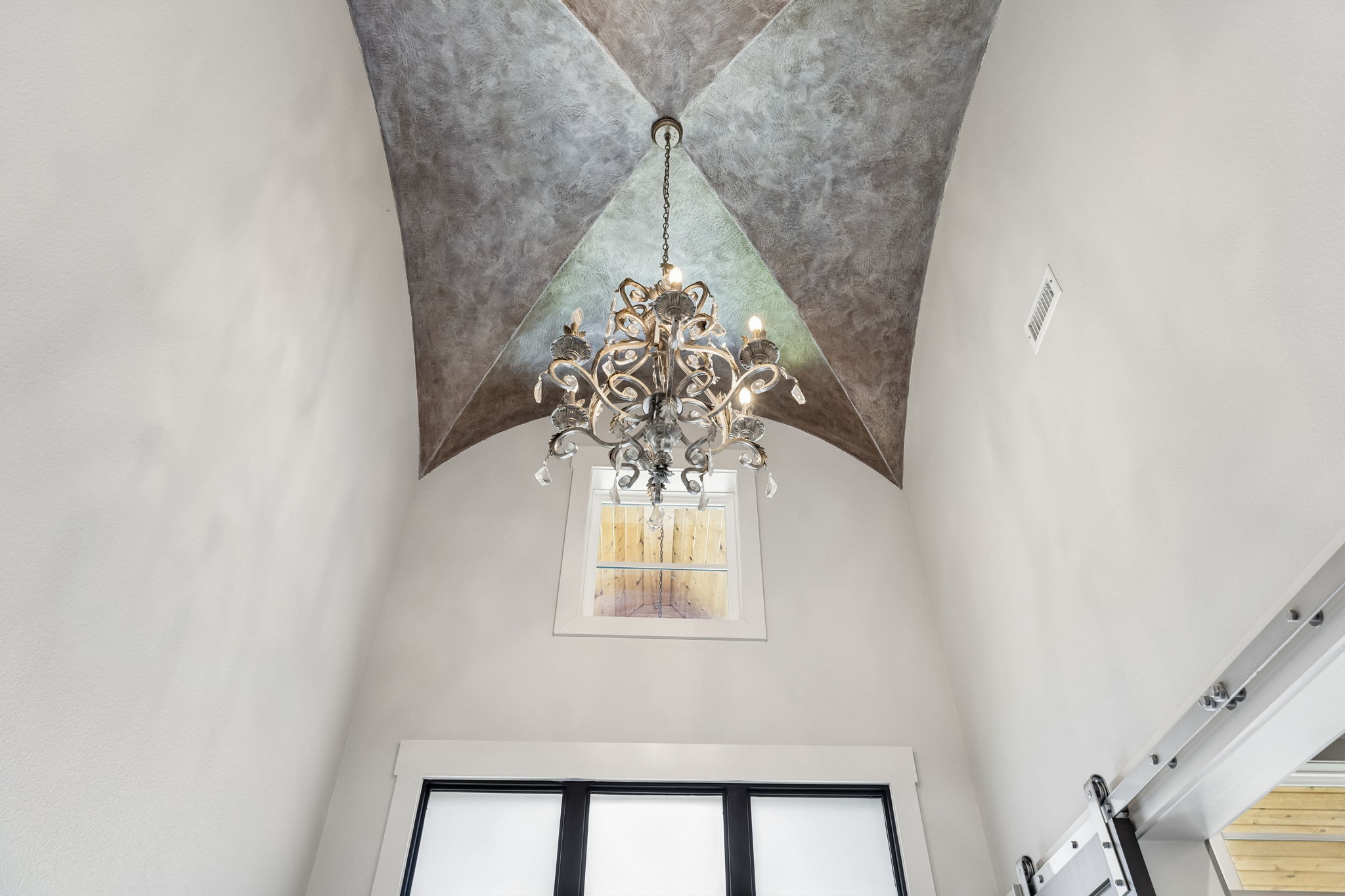 A Statement Ceiling Over the Entry – The soaring foyer is capped by a sculptural ceiling treatment and chandelier, adding architectural drama well before the main living spaces come into view.
