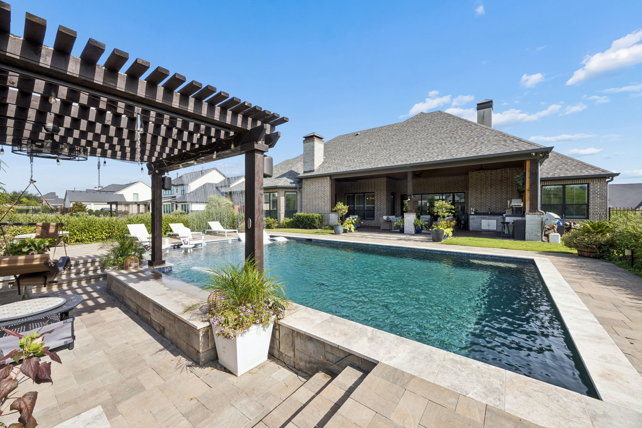 An Outdoor Setting That Feels Complete – From the covered terrace and outdoor kitchen to the pool, pergola, and layered landscaping, every part of the backyard is designed to be used and enjoyed.