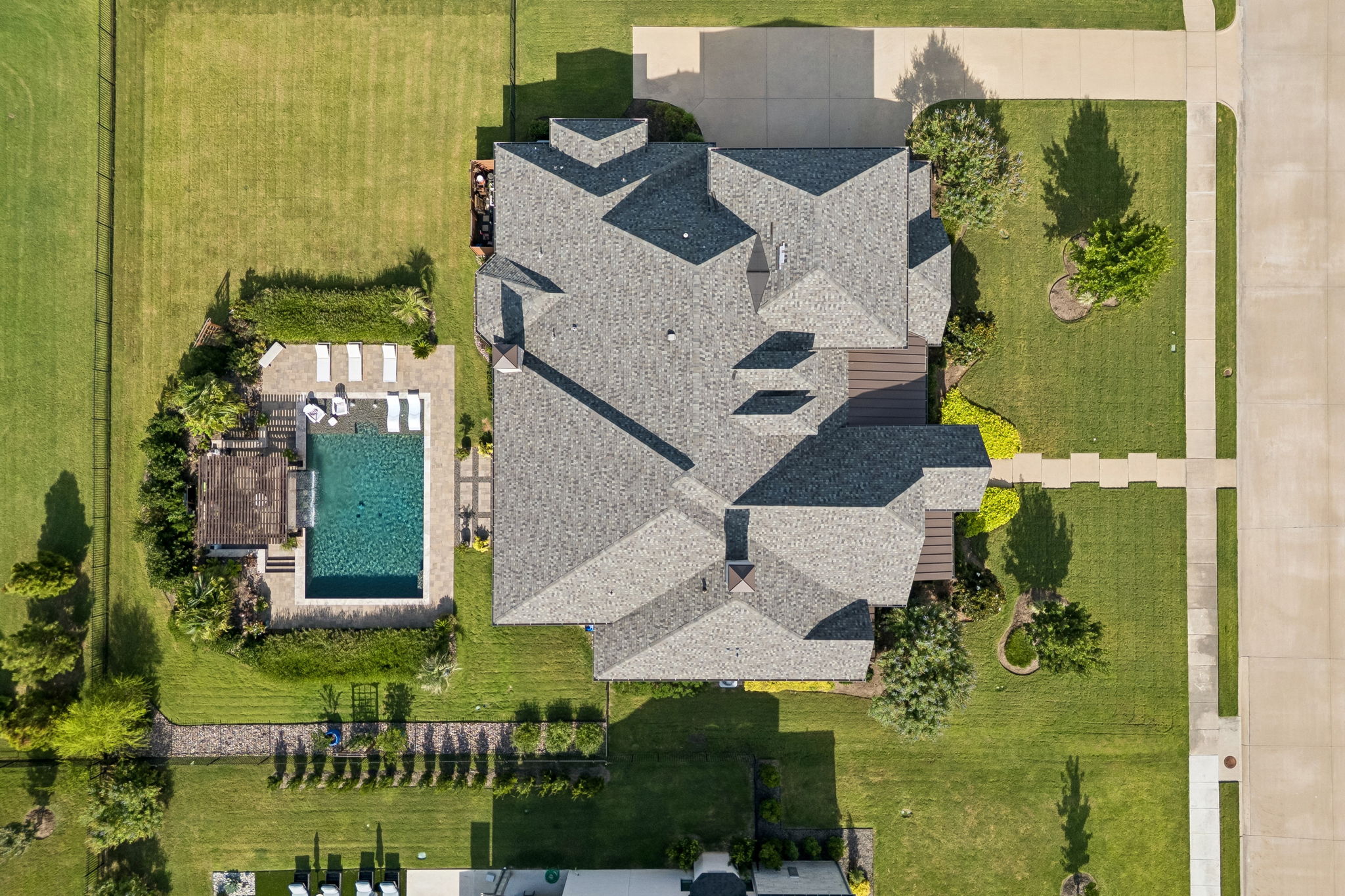 A Property Planned for Both Beauty and Function – This aerial view shows how the home, three-car side-entry garage, covered terraces, pool, pergola, lawn, and landscaping are thoughtfully arranged across the homesite.