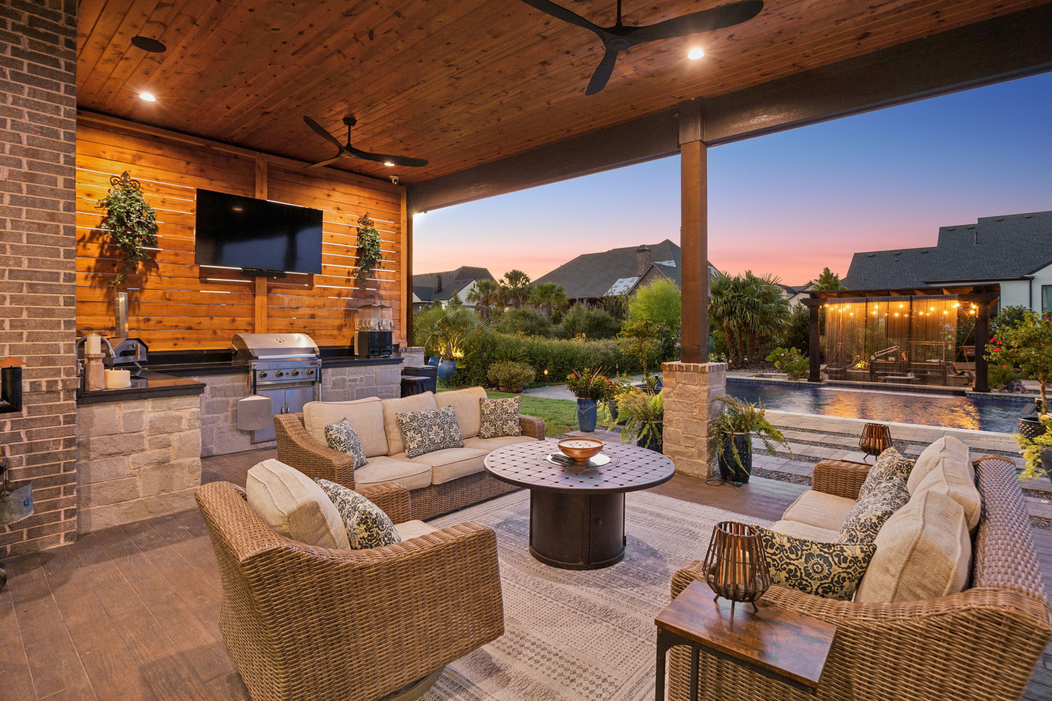 Outdoor Living That Shines After Dark – The covered terrace becomes an evening gathering space with warm lighting, an outdoor kitchen, views of the illuminated pergola, and easy access to the pool.