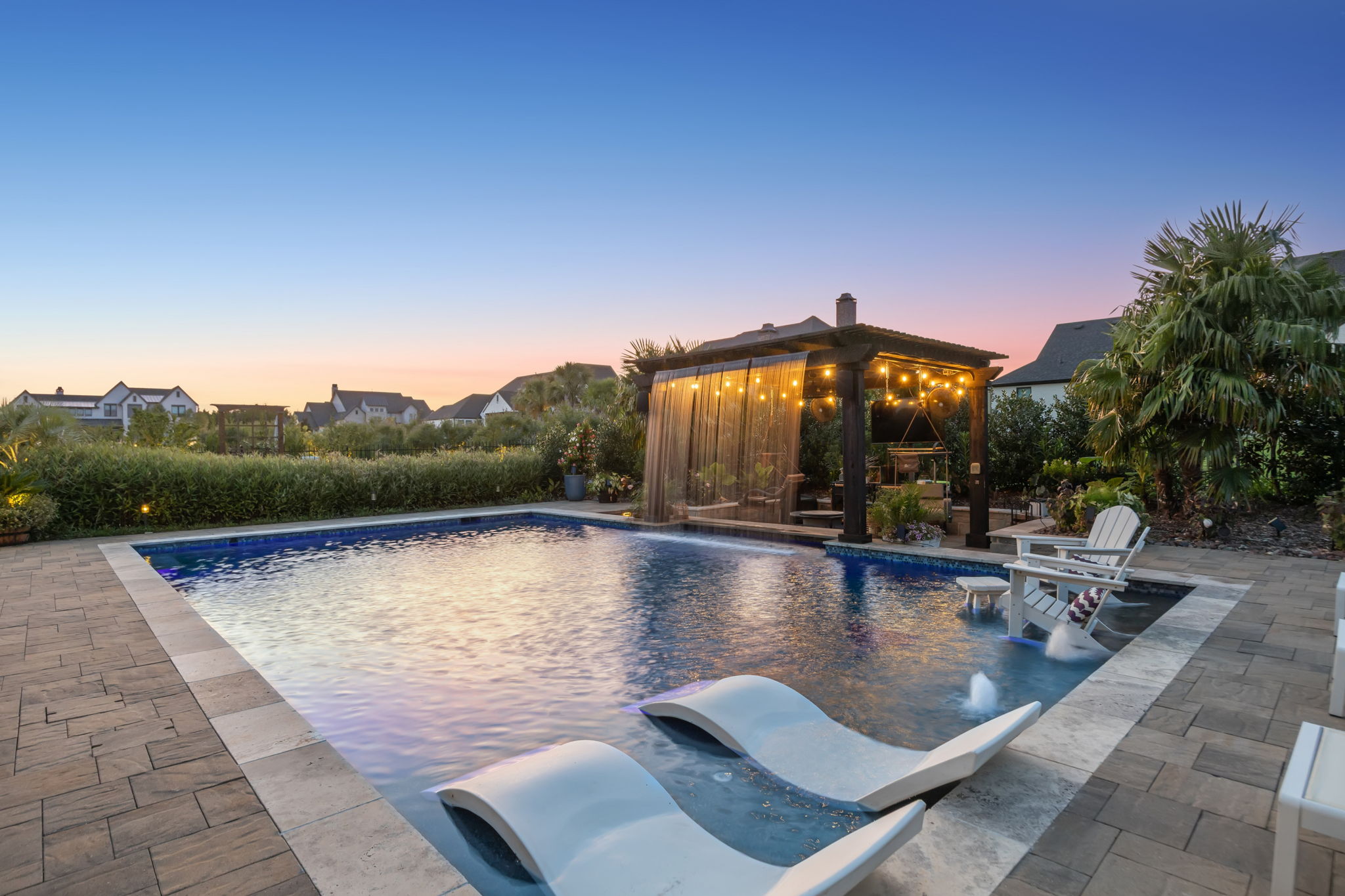 A Resort Setting from Day into Evening – Pool lighting, illuminated water features, and string lights across the pergola create a relaxing atmosphere for nighttime swimming and outdoor entertaining.