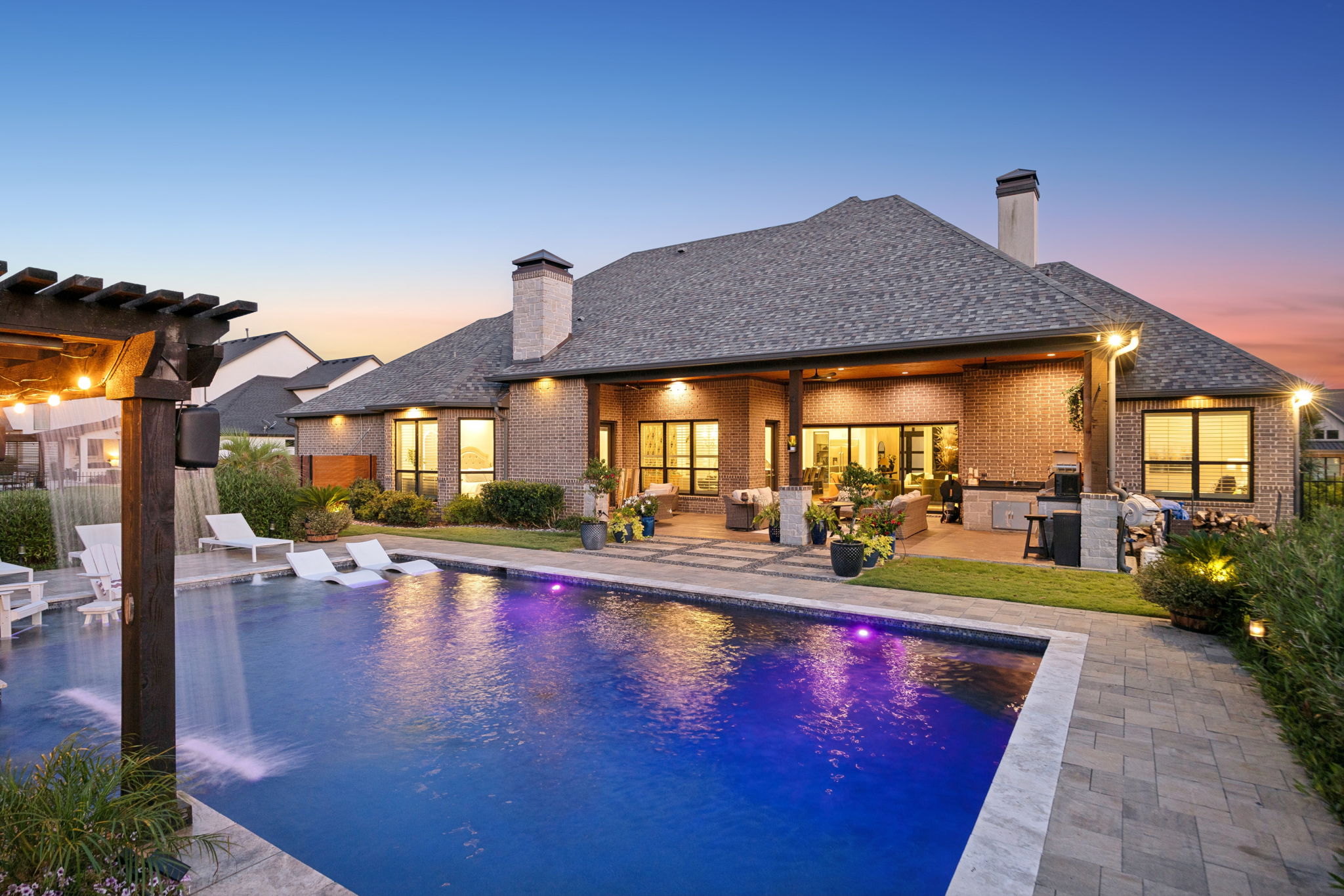 A Backyard Designed to Glow at Night – Illuminated water, layered landscape lighting, and the covered terrace create an inviting setting for swimming, dining, and relaxing well into the evening.