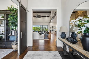 A Direct View into the Heart of the Home – The entry opens toward the main living area, immediately revealing the home’s open layout, hand-scraped hardwood flooring, exposed beams, and connection to the outdoor living spaces beyond.
