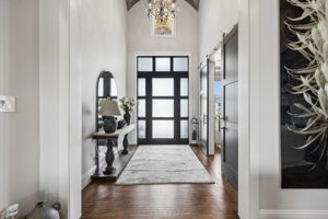 A Dramatic, Light-Filled Entry – A contemporary glass-paneled front door, soaring ceiling, statement lighting, and wide interior openings set the tone for the custom architectural details found throughout the home.