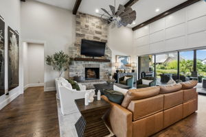 A Great Room Designed Around the View – The spacious living area is anchored by a two-story stone fireplace and framed by exposed beams, while the retractable glass wall extends the room visually and functionally toward the covered terrace and pool.