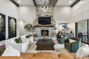 An Inviting Fireplace Focal Point – The full-height stone fireplace, raised hearth, wood mantel, and exposed ceiling beams give the great room a strong architectural centerpiece while maintaining generous space for multiple seating arrangements.