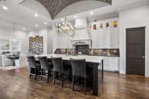 A Statement Kitchen Built for Gathering – An oversized quartz-topped island offers extensive prep space and counter seating, while custom cabinetry, dramatic stone surfaces, and a brick-vaulted ceiling.