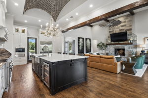 A Strong Visual Connection Between Kitchen and Great Room – The oversized island anchors the open layout, while the brick-vaulted ceiling, exposed beam, and stone fireplace create a seamless transition.