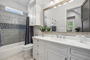 A Secondary Bath with Thoughtful Finishes – A long quartz-topped vanity provides generous counter and storage space, while the tub-shower combination features large-format tile, a decorative accent band, and natural light.