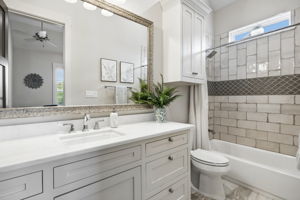 A Private Bath with Custom Tilework – The ensuite bath features a long quartz-topped vanity, abundant cabinetry, a tiled tub-shower surround, decorative accent detail, and a high window that brings in natural light.