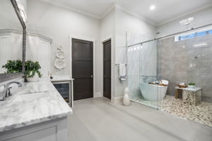 A Spa-Inspired Wet Room – The primary bath features a glass-enclosed wet room with a freestanding soaking tub, multi-head shower, pebble flooring, textured tile, and natural light for a relaxing retreat at home.