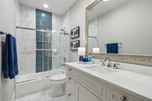 A Bright Full Bath with Bold Accent Tile – The upstairs bath pairs a long vanity and quartz counter with a tub-shower surround featuring marble-look tile and a vertical blue mosaic accent.