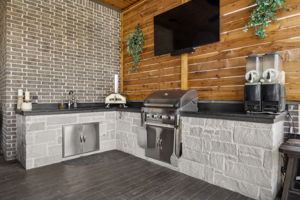 A Fully Equipped Outdoor Kitchen – Built-in grilling, a sink, extensive counter space, storage, and a mounted television make this area ready for casual meals, game days, and effortless poolside entertaining.