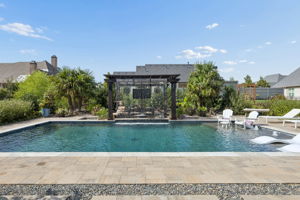 A Resort-Style Pool with Multiple Ways to Enjoy It – The spacious pool includes a broad swimming area, in-water loungers, shallow seating, and water features framed by pavers and lush landscaping.