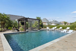 A Backyard Built Around Relaxation – The pool, pergola, sun shelf, and surrounding lounge areas create distinct places to swim, unwind, gather, or enjoy the garden setting.