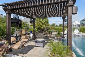 A Pergola Retreat Beside the Water – The cedar pergola adds another shaded destination with hanging seating, string lights, fans, and a dramatic curtain of water along the pool’s edge