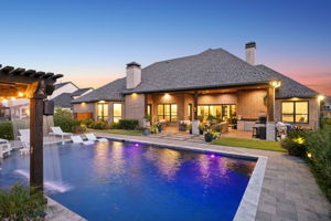 A Backyard Designed to Glow at Night – Illuminated water, layered landscape lighting, and the covered terrace create an inviting setting for swimming, dining, and relaxing well into the evening.
