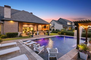 Twilight Views Across the Pool – The home’s rear elevation, covered outdoor living area, and illuminated pool come together in a polished resort-style setting.