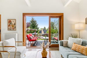 With the French doors wide open, the living room lets in a gentle breeze and the sweet scent of the garden. A glimpse of the front door and the staircase leading to the primary bedroom loft adds to the serene, inviting flow.