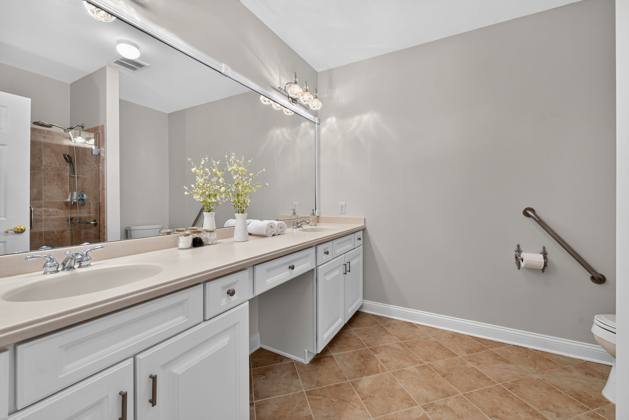 The private bath is freshly painted and features a double-sink vanity with makeup counter, seated shower with frameless shower door, and ceramic tile flooring.