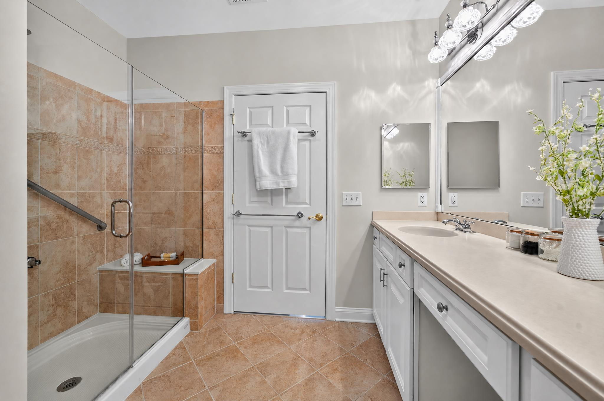 The private bath is freshly painted and features a double-sink vanity with makeup counter, seated shower with frameless shower door, and ceramic tile flooring.