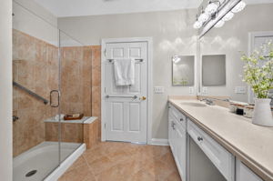 The private bath is freshly painted and features a double-sink vanity with makeup counter, seated shower with frameless shower door, and ceramic tile flooring.