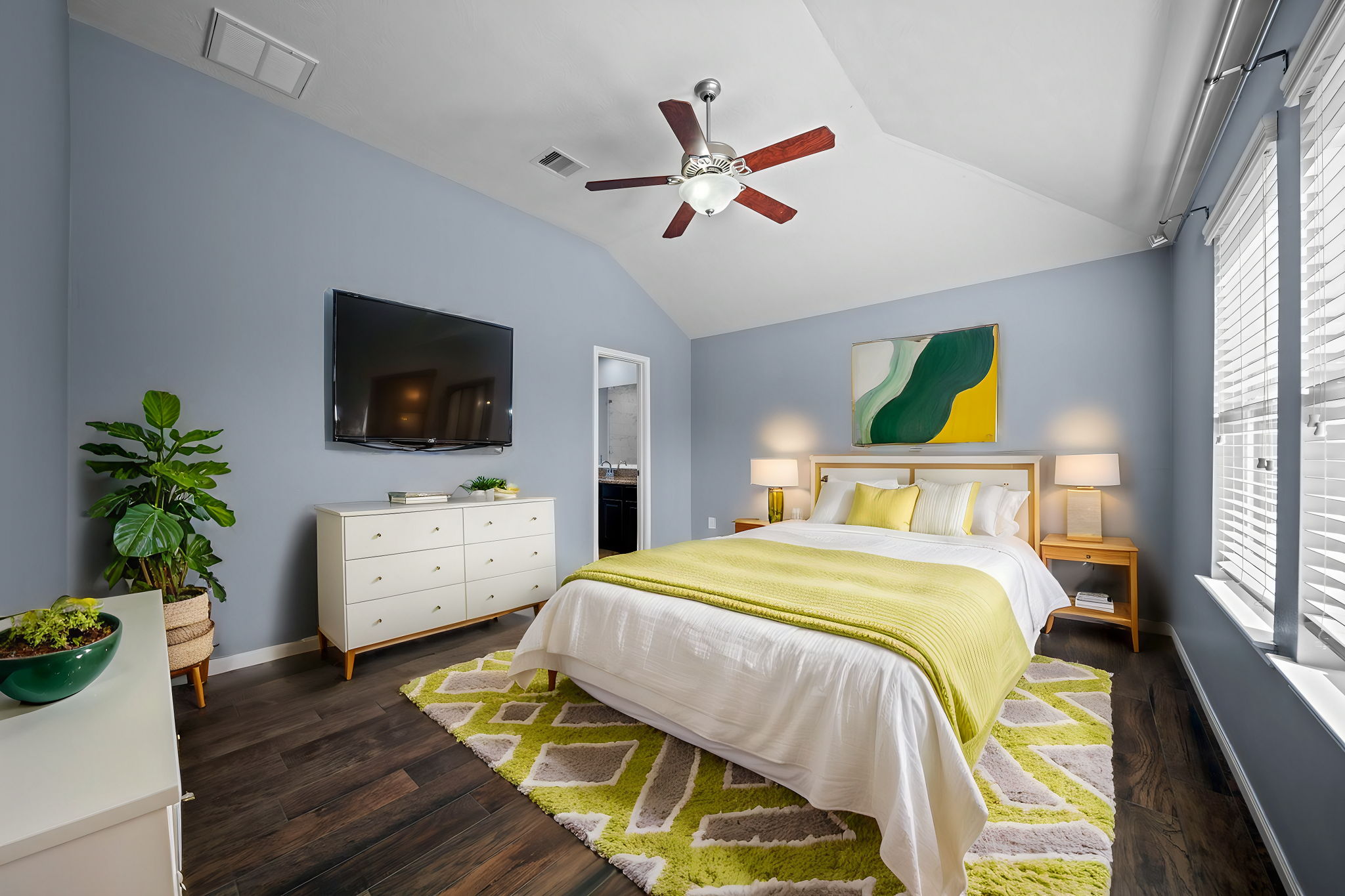 Primary bedroom with high ceilings, a ceiling fan, 2" blinds, wood-look tile flooring, 2" blinds and an en-suite.