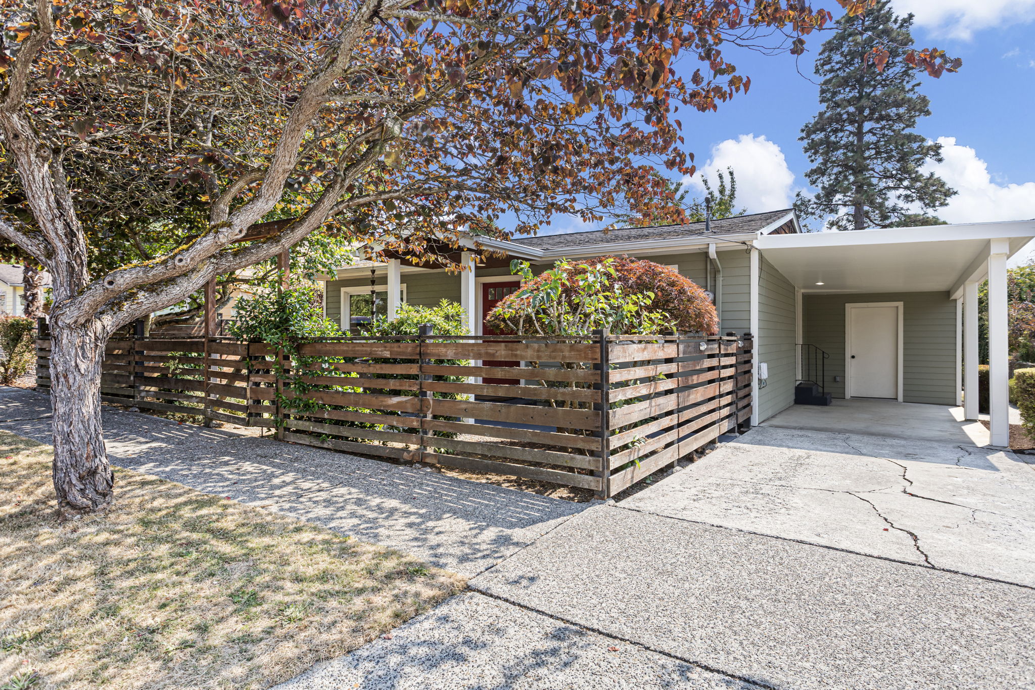 One last look from the practical side: attached covered parking sits right beside the house, while the fenced front garden keeps the arrival feeling residential rather than driveway-first.