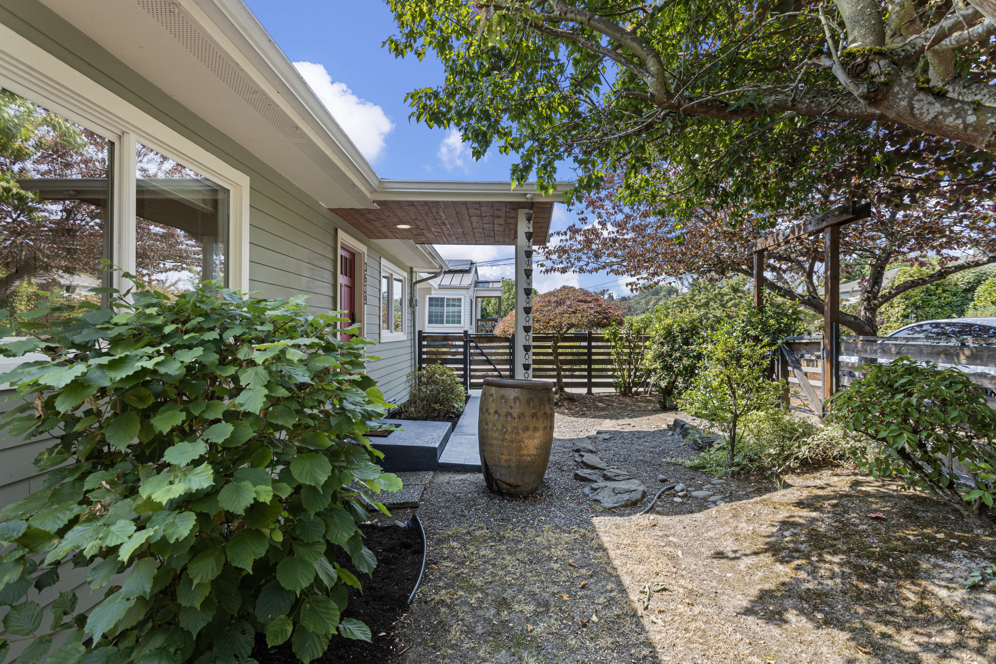 Inside the fence, gravel, stone, sculptural plantings and mature canopy give the front grounds a distinctly Japanese-garden feel.